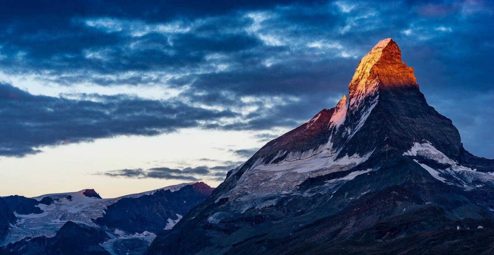 Dramatic mountain peak at sunrise with glowing summit and rugged terrain under a vibrant sky, perfect for nature and travel themes.