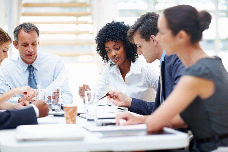 Colleagues in a board meeting discussing documents and using tablets, highlighting teamwork and collaboration.