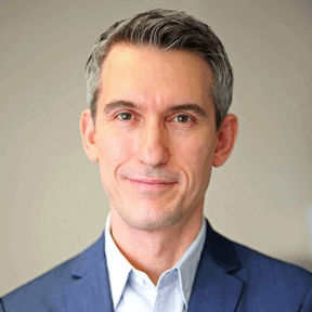 Professional portrait of a man in a blue suit, light background, business attire, corporate headshot, confident expression.