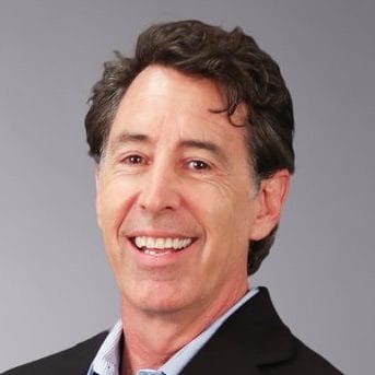 I don't know who this person is. Smiling man with dark hair wearing a suit against a gray background.