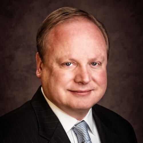 I don't know who this is. Professional man in suit and tie, smiling, with a neutral background, ideal for business profile or corporate use.