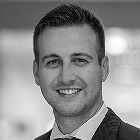 Professional headshot of a smiling man in a suit, black and white portrait, business profile photo.