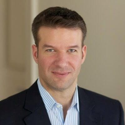 I don't know who this person is. Professional man in a suit, light blue shirt, smiling, neutral background.