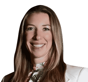 Headshot of a smiling woman with long hair, wearing a white blazer and floral top, isolated on a black background.