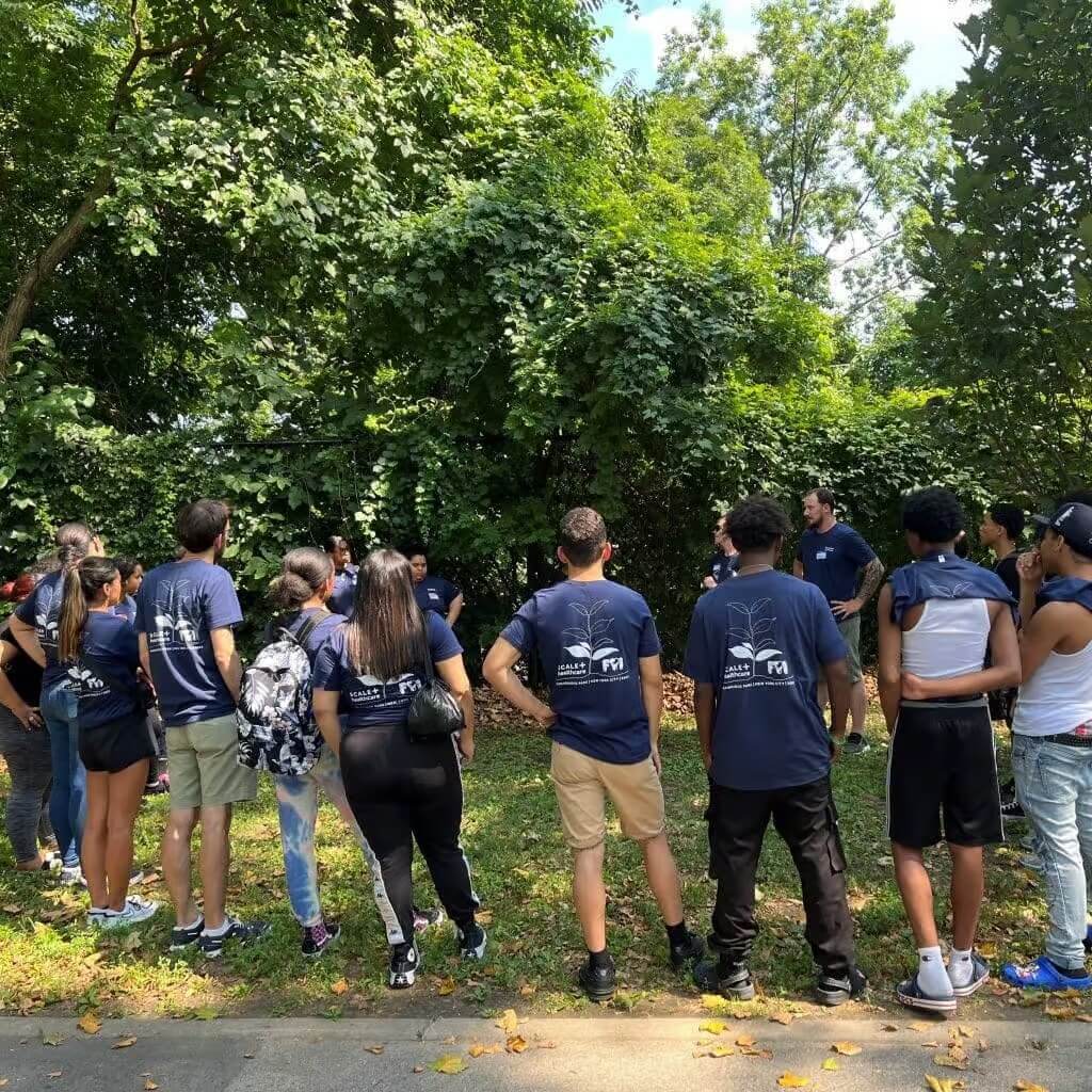 Group of people in blue shirts engage in outdoor team-building activity surrounded by lush greenery.