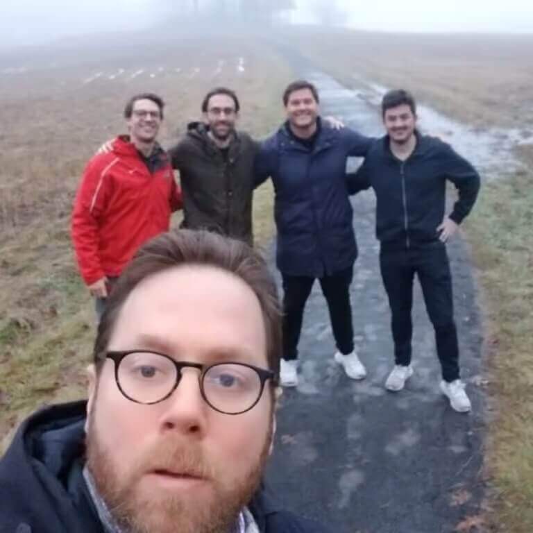 Group of five men posing during a foggy team hike on a rural path.