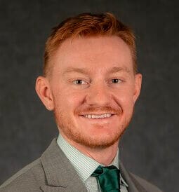 Professional man in a suit with a grey background, smiling, red hair, green tie, business portrait.