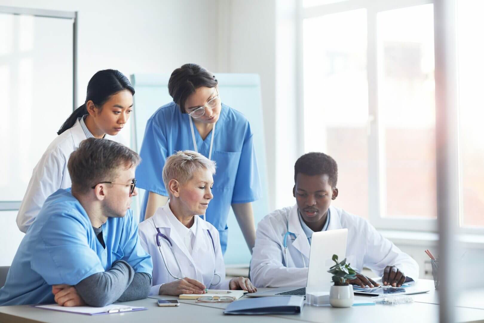 Group of diverse doctors collaborating on laptop in bright medical office.