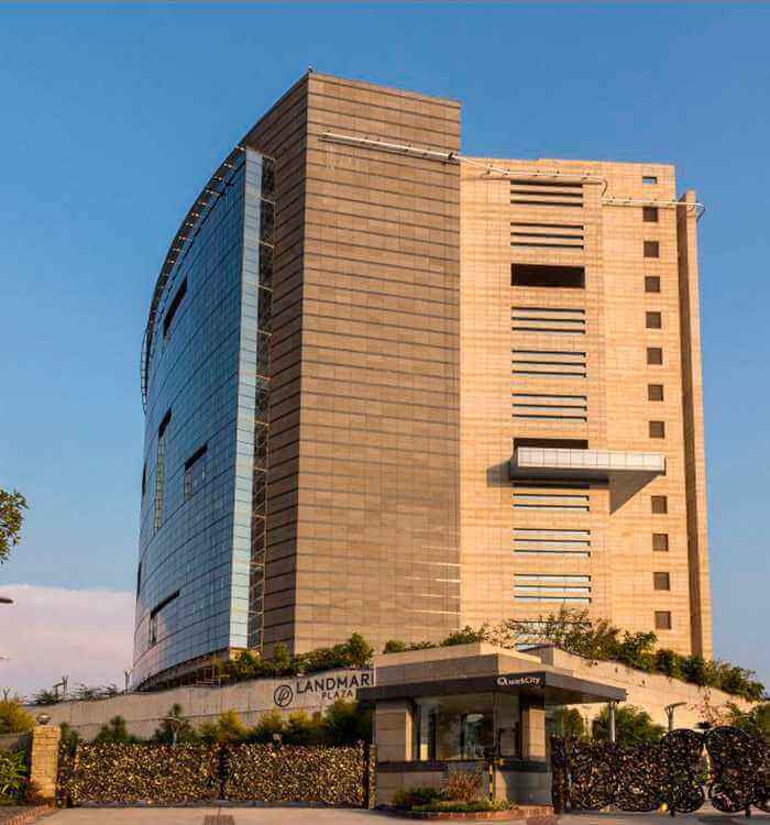 Modern commercial building Landmark Plaza with glass facade, clear sky, and greenery in urban setting.