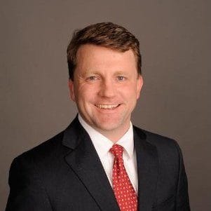 I don't know who this person is, but he is wearing a suit and tie, smiling against a neutral background.
